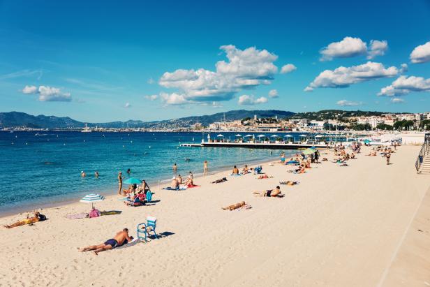 Ein sonniger Strand mit Menschen, die sich sonnen und im Meer schwimmen.