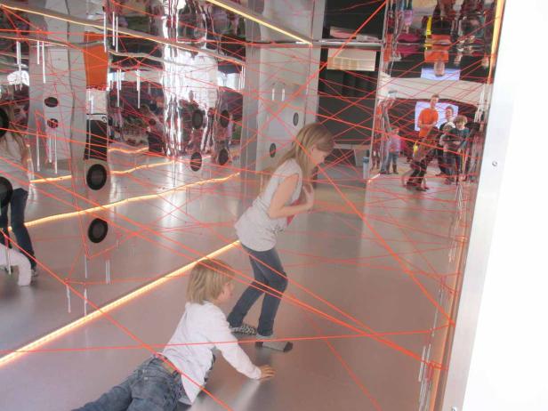 Zwei Kinder spielen in einem Raum mit einem Netz aus roten Seilen.