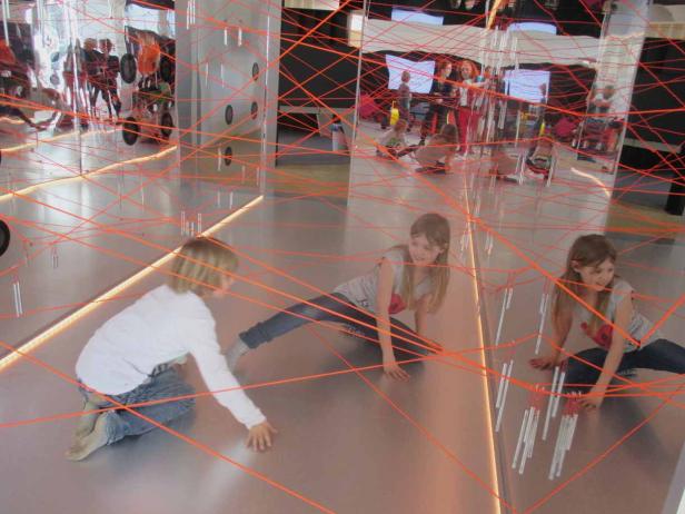 Kinder spielen in einem Raum mit einem Netz aus orangefarbenen Seilen.