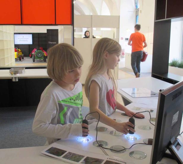 Zwei Kinder betrachten mit beleuchteten Lupen Objekte auf einem Tisch.