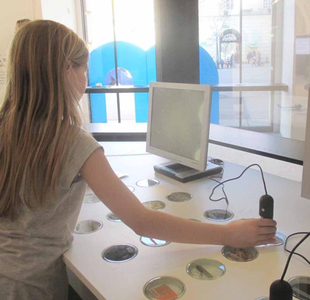 Ein Mädchen interagiert mit einer interaktiven Ausstellung mit einem Bildschirm und runden Behältern.