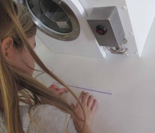 Ein Mädchen betrachtet eine Sequenz von DNA-Basen auf einem weißen Untergrund.