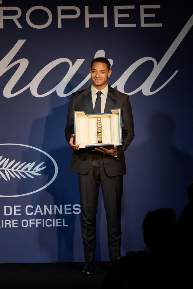 Ein Mann im Anzug hält die Trophäe des Filmfestivals von Cannes.