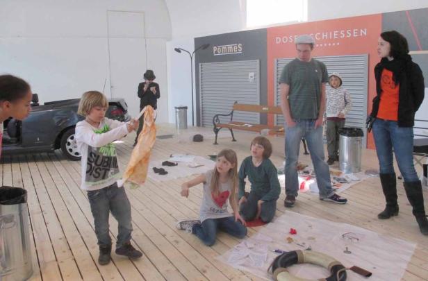 Eine Gruppe von Kindern und Erwachsenen in einem Raum mit Requisiten und einer Installation.