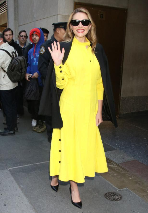 Elizabeth Olsen trägt einen gelben Zweiteiler und winkt.