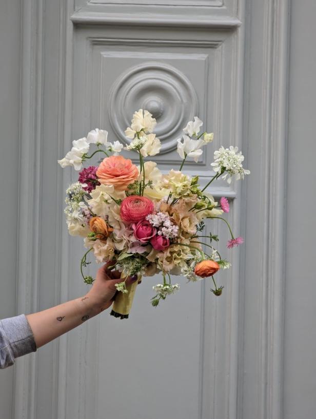 Eine Hand hält einen bunten Blumenstrauß vor einer grauen Tür.