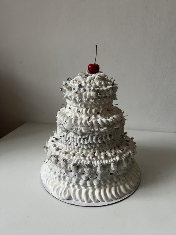 Ein dreistöckiger Kuchen mit weißer Glasur und einer Kirsche auf der Spitze.