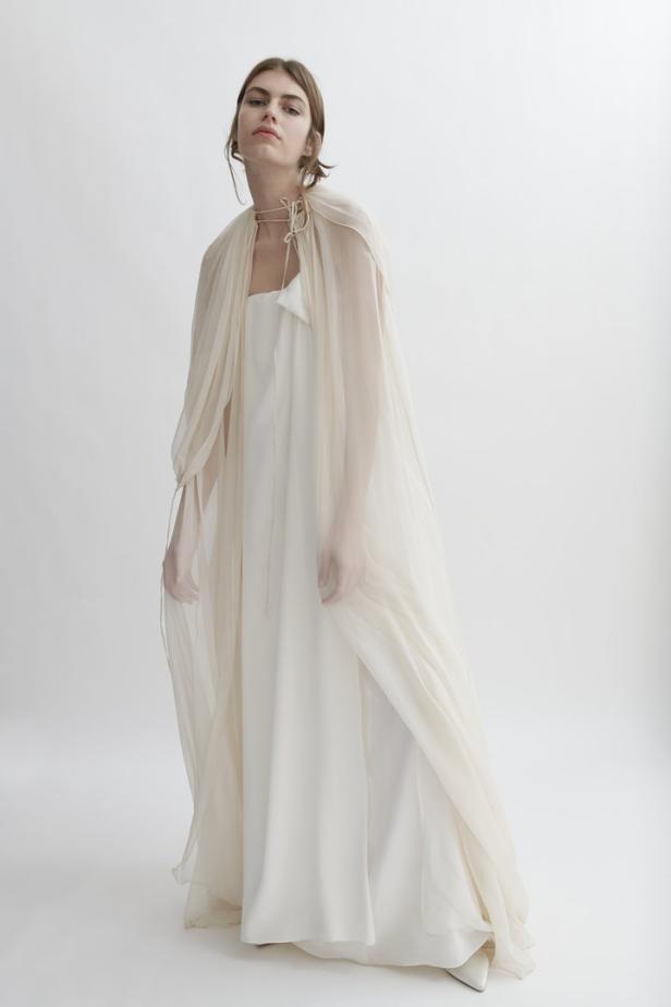 Eine Frau trägt ein elfenbeinfarbenes Kleid mit einem transparenten Überwurf.