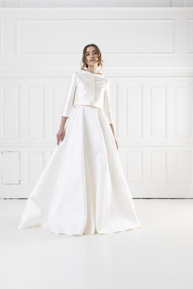 Eine Frau in einem eleganten, zweiteiligen weißen Kleid vor einer weißen Wand.