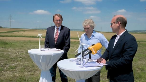 Drei Personen stehen an Tischen mit Windradmodellen in einer ländlichen Umgebung.