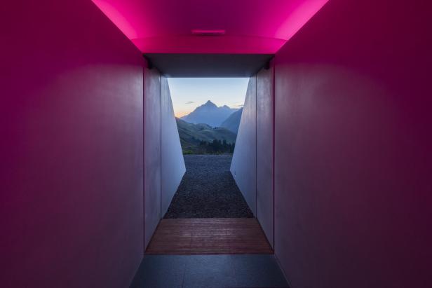 Ein Tunnel mit rosa Beleuchtung führt zu einer Berglandschaft.