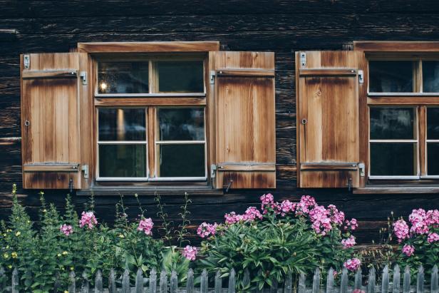 Blumen blühen vor einem hölzernen Haus mit Fensterläden.