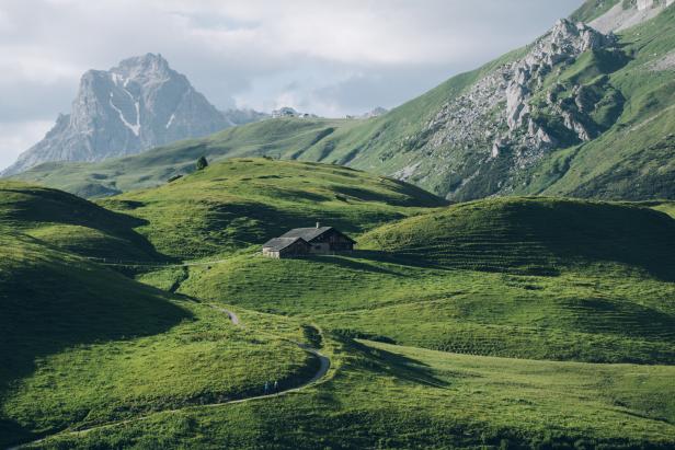 Eine Hütte liegt auf einer grünen Wiese in den Bergen.