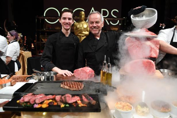 Zwei Köche präsentieren Steaks und rohes Fleisch vor dem Hintergrund der Oscar-Verleihung.