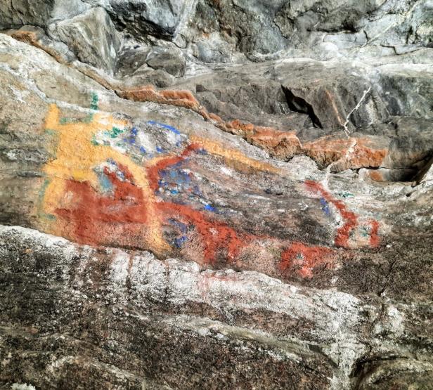 Auf einer Felswand sind rote, gelbe und blaue Malereien zu sehen.