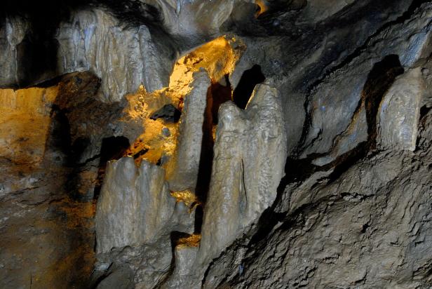 Verschiedene Stalagmiten ragen in einer dunklen Höhle empor.