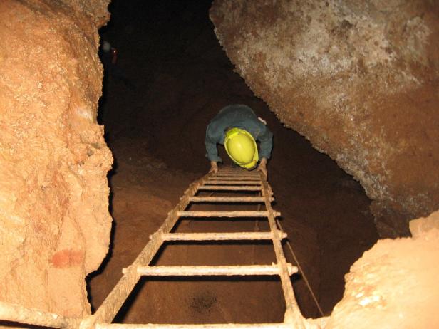 Ein Mann mit gelbem Helm steigt eine Leiter in einer Höhle hinab.