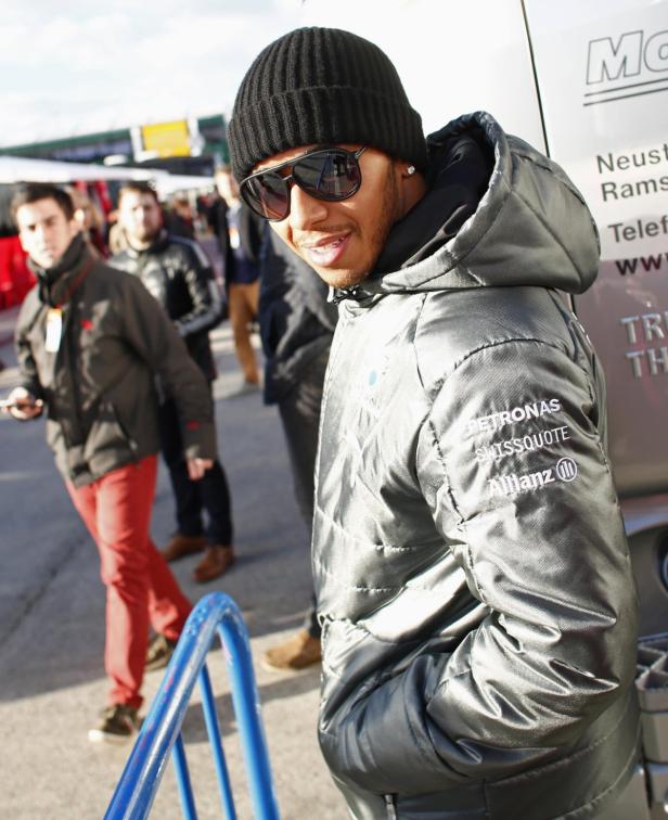 Lewis Hamilton mit Mütze und Sonnenbrille vor einem Rennwagen.