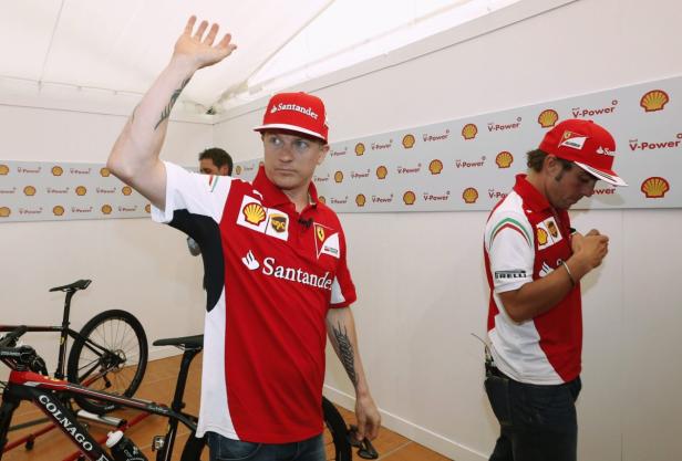 Kimi Räikkönen grüßt mit erhobener Hand, während ein anderer Mann im Ferrari-Teamoutfit zu sehen ist.