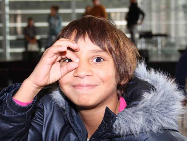 Ein lächelnder Junge mit Winterjacke formt mit seiner Hand eine Art „Ok“-Zeichen vor seinem Auge.