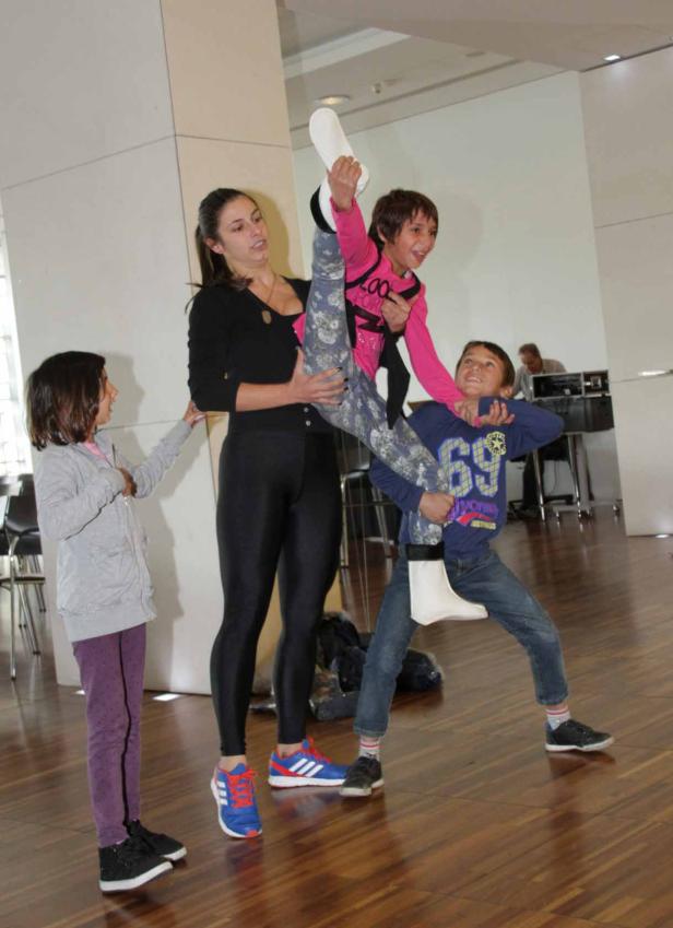 Eine Frau hält ein Kind mit ausgestrecktem Bein, während ein anderes Kind es stützt.