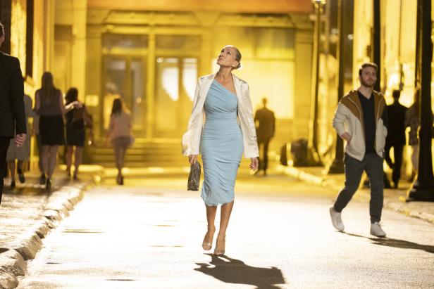 Sarah Jessica Parker in einem hellblauen Kleid auf einer gelb beleuchteten Straße.