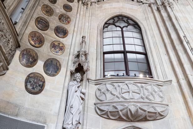 Eine Statue und Wappen schmücken die Wand neben einem gotischen Fenster.