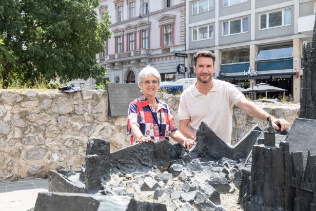 Eine ältere Frau und ein Mann stehen an einem Stadtmodell aus Bronze.