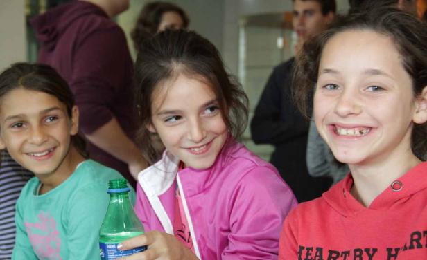 Drei lächelnde Mädchen stehen zusammen, eines hält eine grüne Plastikflasche.