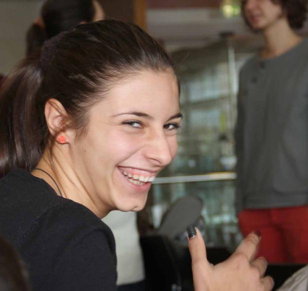 Eine junge Frau mit Pferdeschwanz lacht in die Kamera.