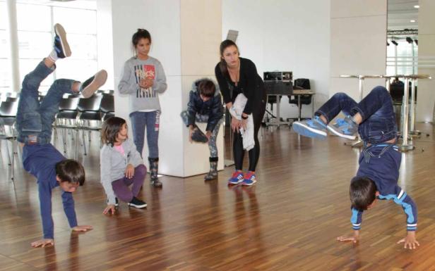Eine Gruppe von Kindern und eine Frau beobachten zwei Jungen, die Handstände machen.