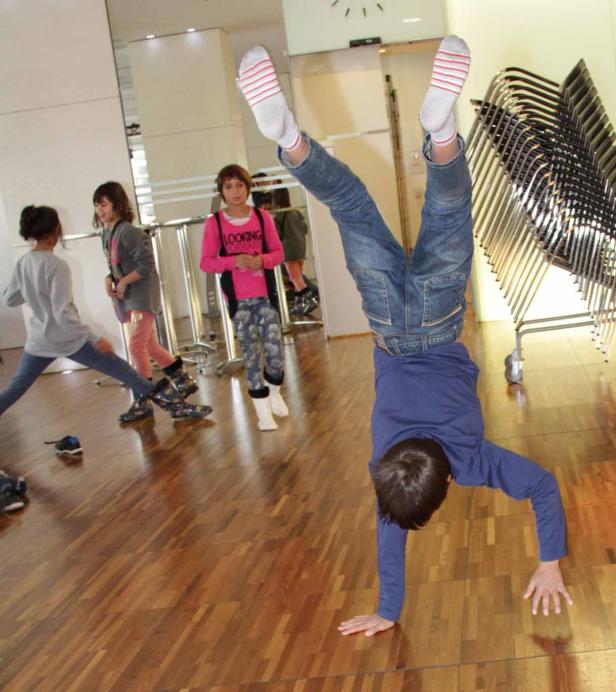 Ein Junge macht einen Handstand in einem Raum mit anderen Kindern.