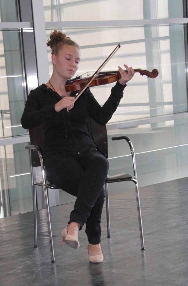 Eine junge Frau sitzt auf einem Stuhl und spielt Geige.