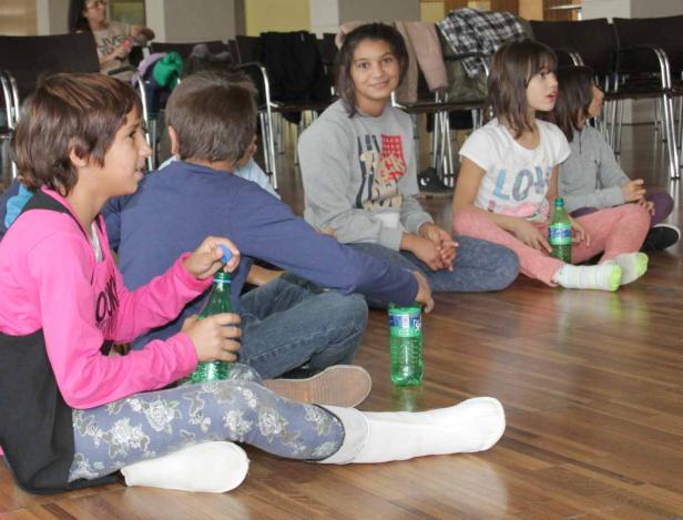 Eine Gruppe von Kindern sitzt auf dem Holzboden und hält Getränkeflaschen.