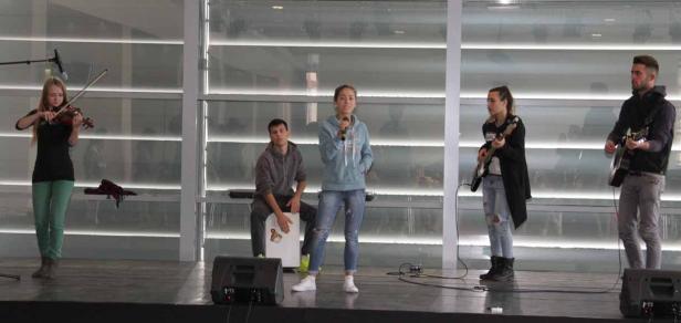 Eine Band spielt auf einer Bühne mit Geige, Gitarren, Cajón und Gesang.