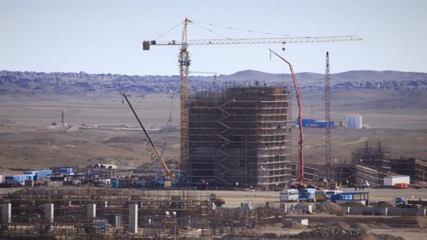 Auf einer Baustelle in einer weiten Landschaft wird ein hohes Gebäude errichtet.