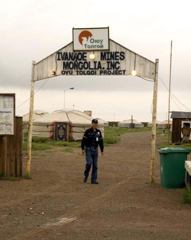 Ein Mann geht durch ein Tor zum Oyu Tolgoi Projekt in der Mongolei, mit traditionellen Jurten im Hintergrund.