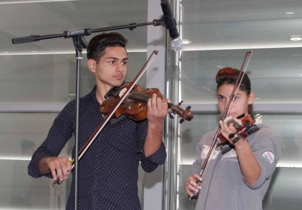 Zwei junge Personen spielen Geige vor einem Mikrofon.