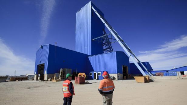 Zwei Arbeiter stehen vor einem großen, blauen Industriegebäude mit Förderturm.