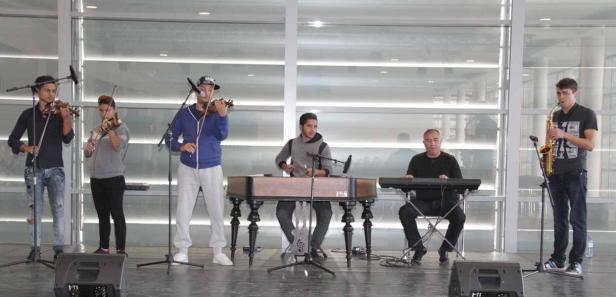 Eine Band spielt auf einer Bühne mit Geigen, Hackbrett, Keyboard und Saxophon.