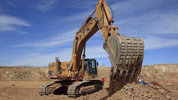 Ein gelber Bagger schaufelt Erde auf einer Baustelle.