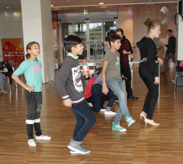 Eine Gruppe von Kindern tanzt in einem hellen Raum auf einem Parkettboden.