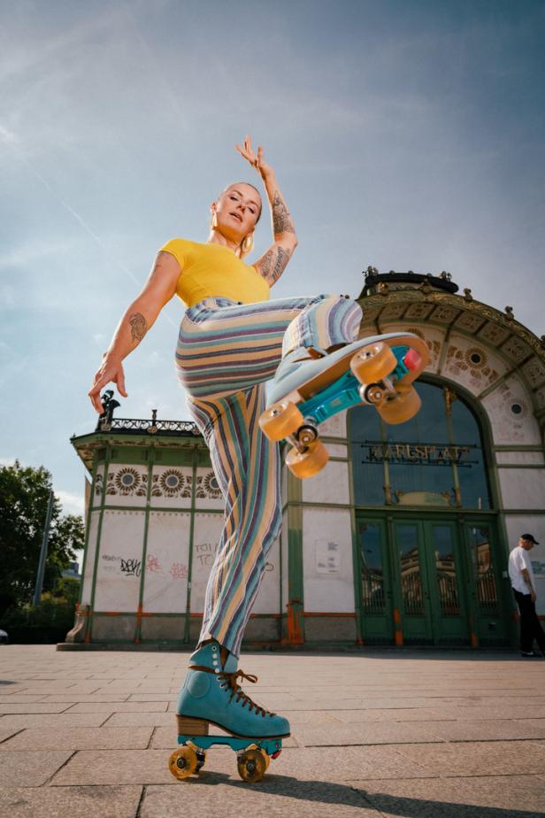 Eine Frau auf Rollschuhen posiert vor dem Karlsplatz in Wien.