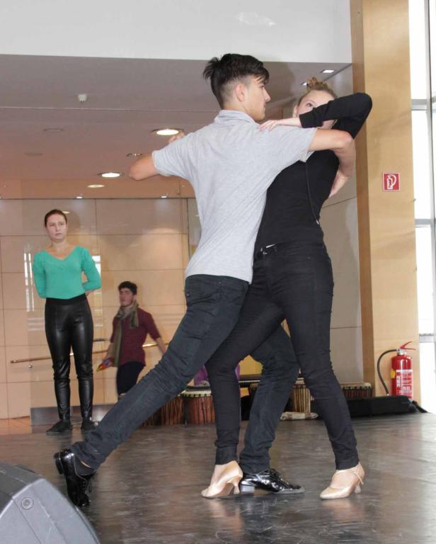 Ein junges Paar tanzt auf einer Bühne, während andere Personen zusehen.