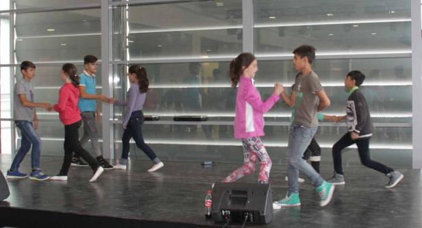 Eine Gruppe von Jugendlichen führt auf einer Bühne ein Spiel mit Händeschütteln auf.