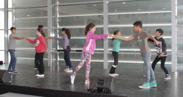 Eine Gruppe von Kindern tanzt auf einer Bühne und hält sich an den Händen.