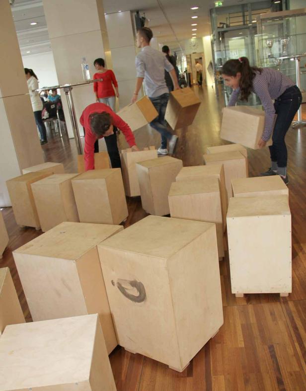 Mehrere Personen tragen und stapeln Holzkisten in einem hellen Raum.