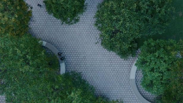 Eine Draufsicht auf einen Platz mit sechseckigen Pflastersteinen, Bäumen und geschwungenen Bänken.