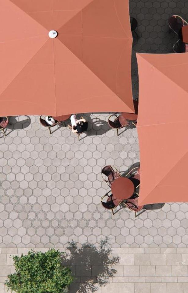 Draufsicht auf einen Außenbereich mit Tischen, Stühlen und Sonnenschirmen auf einem sechseckigen Pflastermuster.