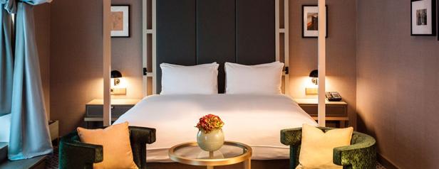 Ein Hotelzimmer mit einem Doppelbett, zwei Sesseln und einem kleinen Tisch mit Blumenstrauß.